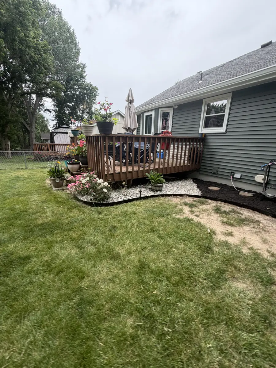Curved backyard mulch beds with roses and potted flowers around wood deck — Kearney MO