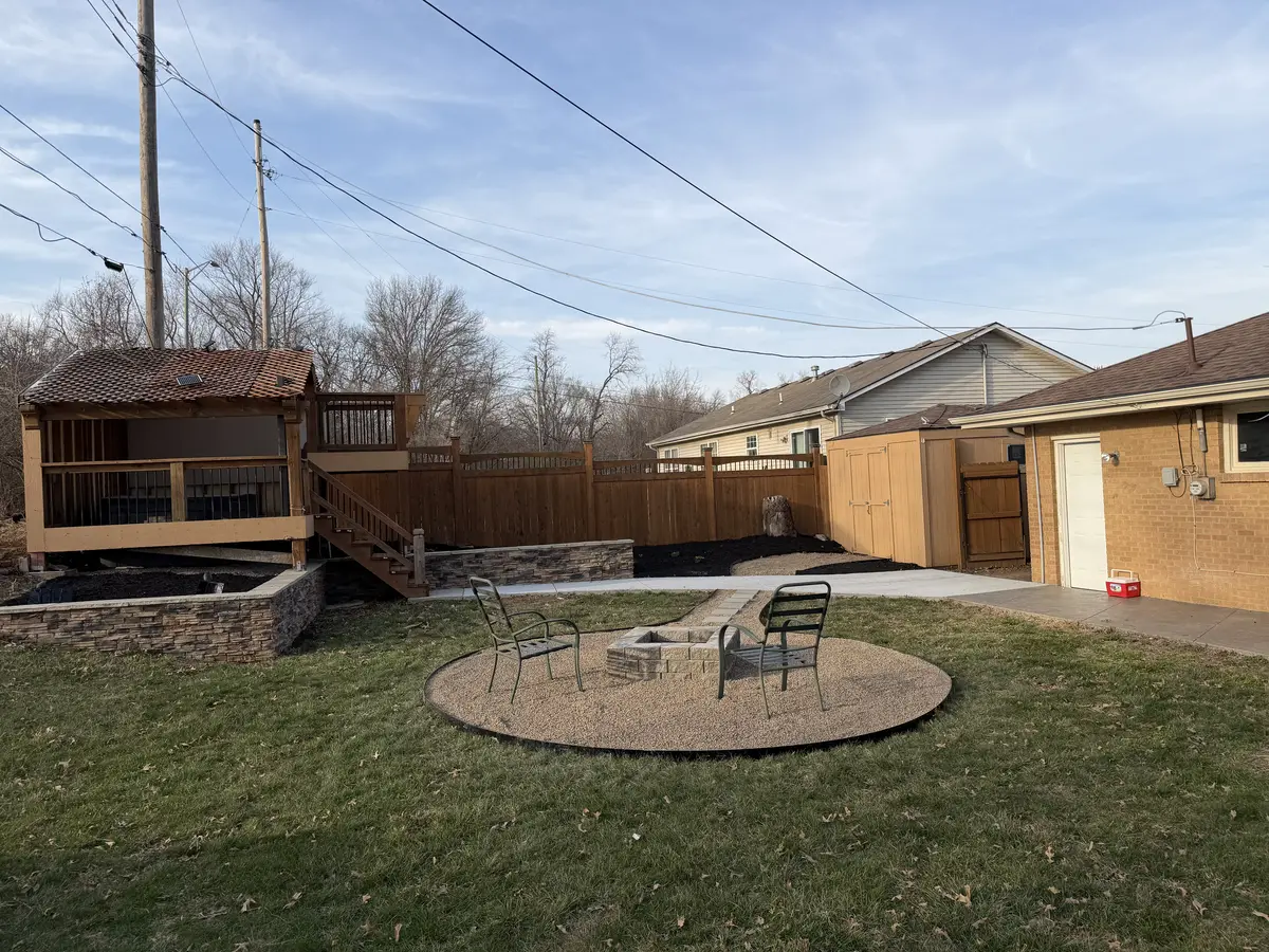 Backyard fire pit patio with gravel pad, cedar gazebo deck, and stone retaining wall — Liberty MO