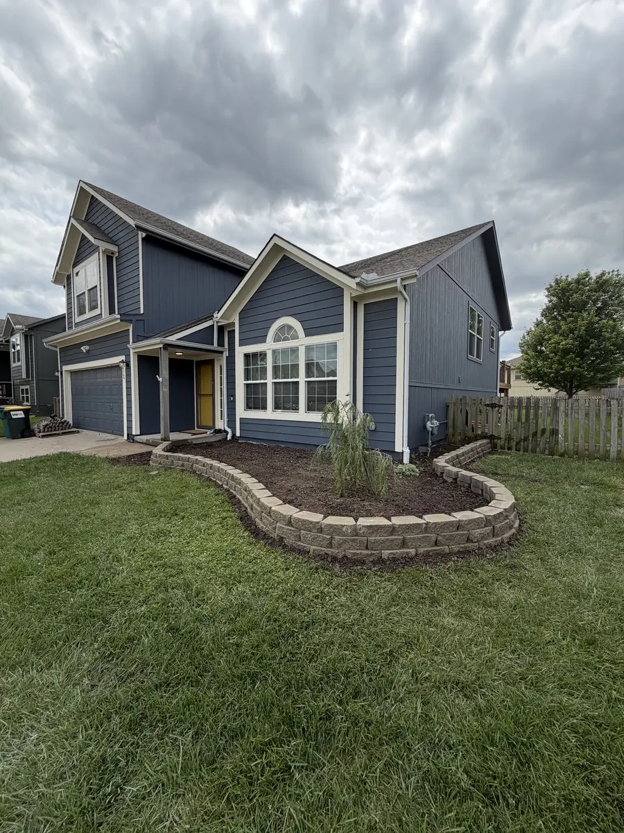 Curved segmental stone retaining wall border along blue two-story home — Kearney MO