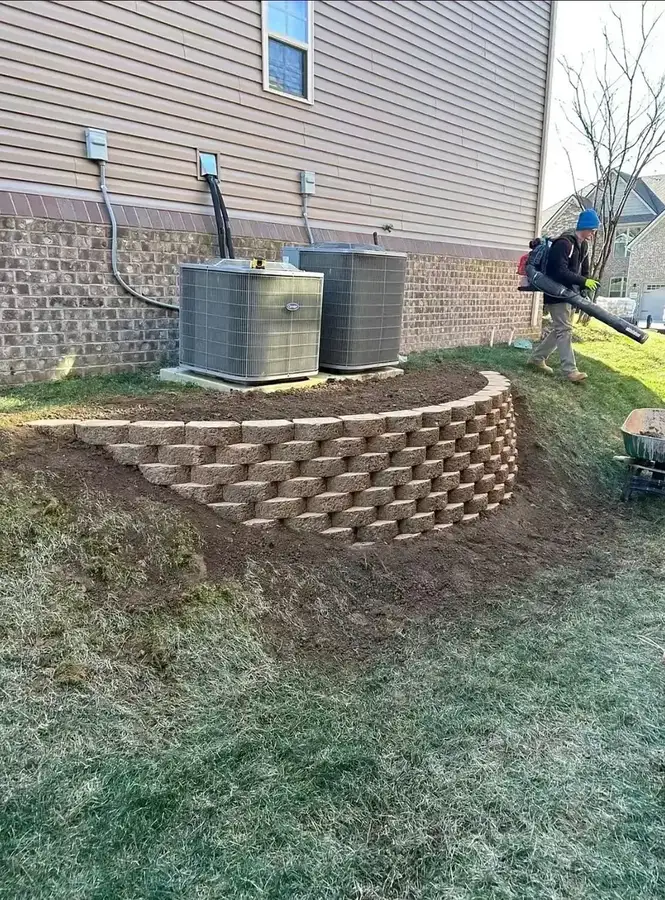 Curved segmental block retaining wall around HVAC units on sloped backyard — retaining wall contractor in Smithville MO