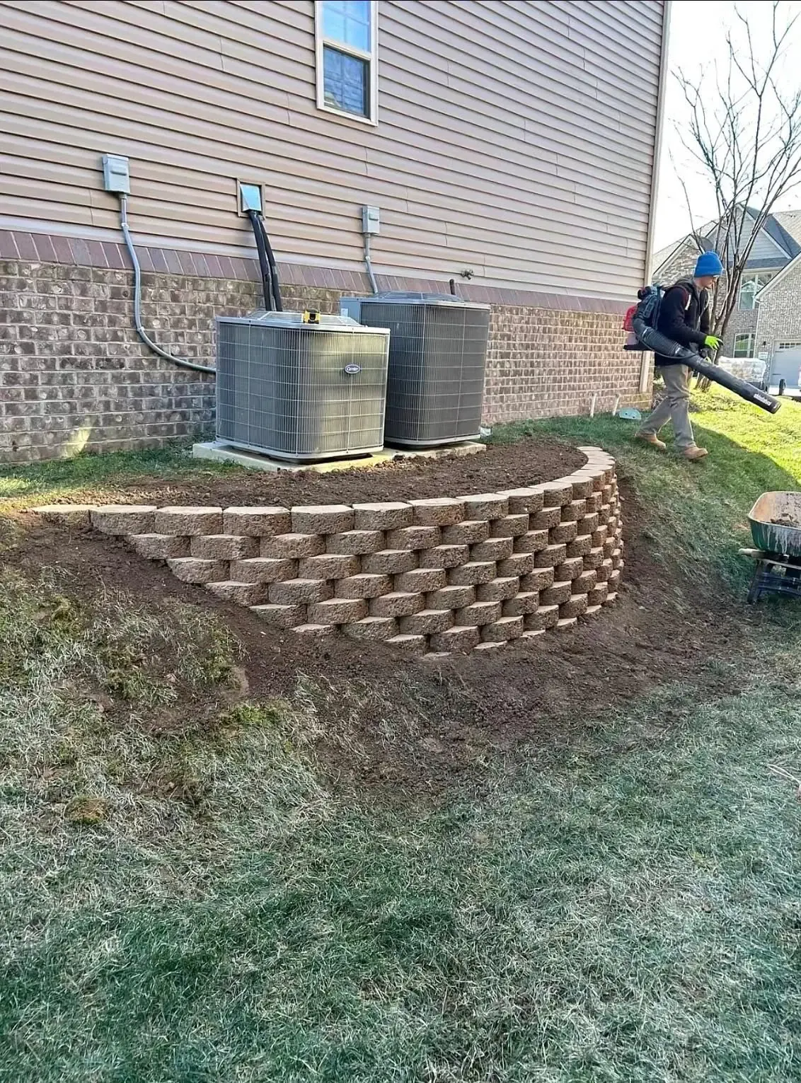 Curved segmental block retaining wall built around HVAC units on sloped backyard — retaining wall contractor in Smithville MO