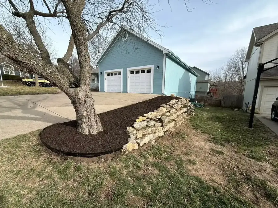 Natural fieldstone retaining wall with mulch bed and tree ring along driveway — retaining walls in Smithville MO