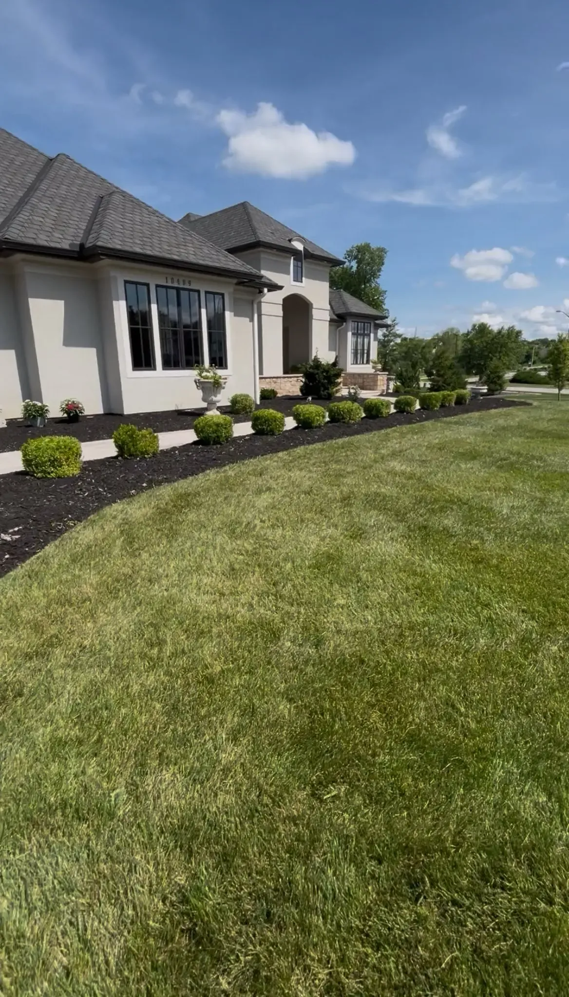 Manicured luxury home front yard with trimmed boxwood shrubs and fresh black mulch beds — landscaping in Smithville MO