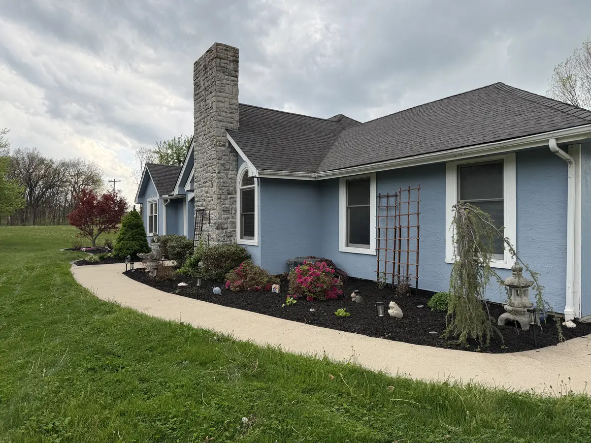 Spring mulch installation with blooming azaleas and weeping tree on blue house — Smithville MO