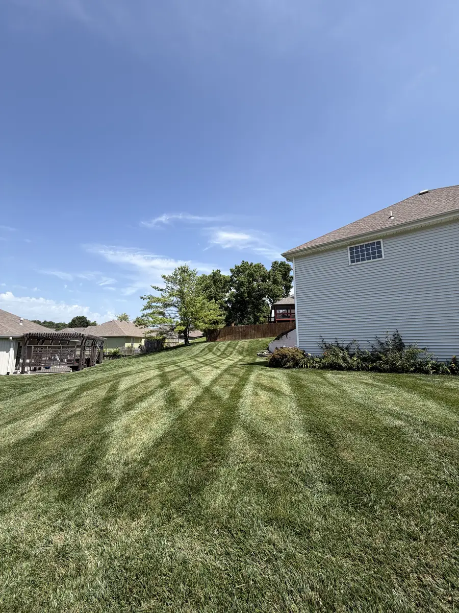 Wide backyard with fan mowing stripes, wooden pergola, and cedar fence — Kearney MO