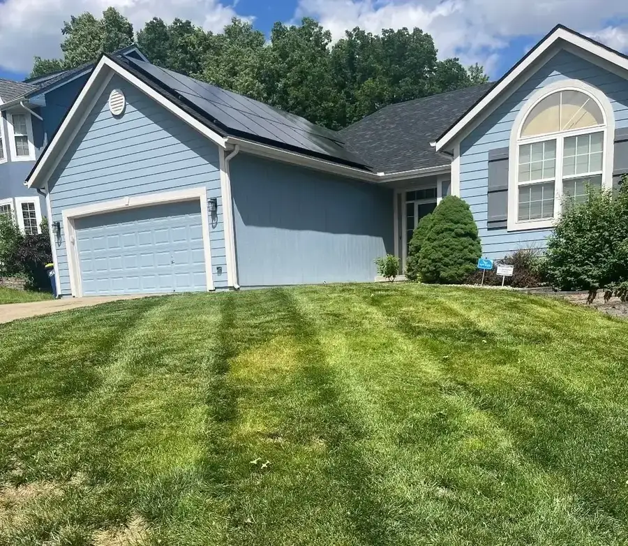 Perfectly striped front lawn at blue house with solar panels — weekly mowing by GC Signature Outdoors in Smithville MO