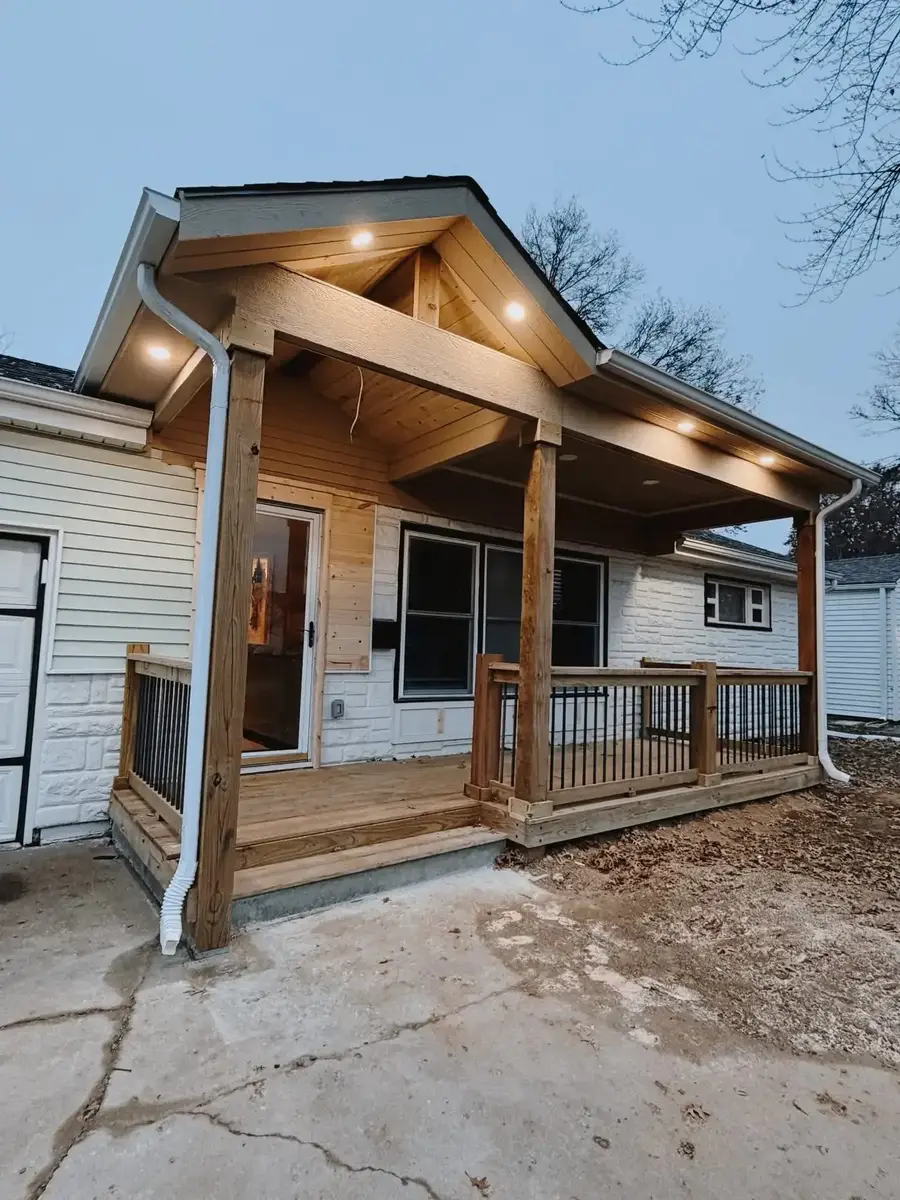 Custom wooden covered front porch with gable roof, recessed lighting, and black railings — outdoor living build Smithville MO